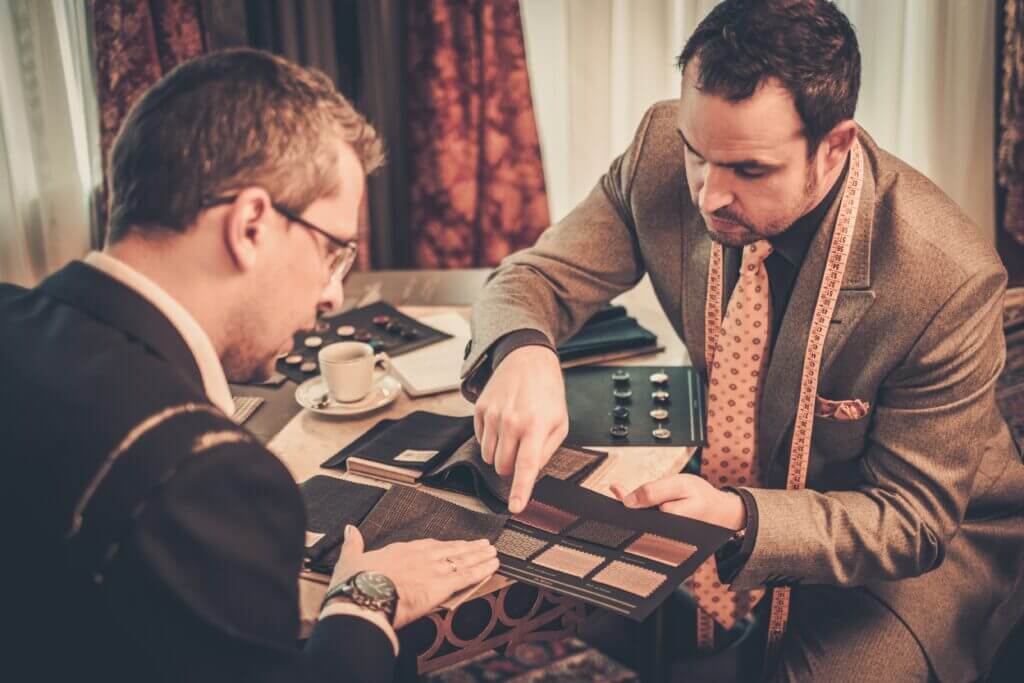 Two male tailors in suits looking through fabric samples